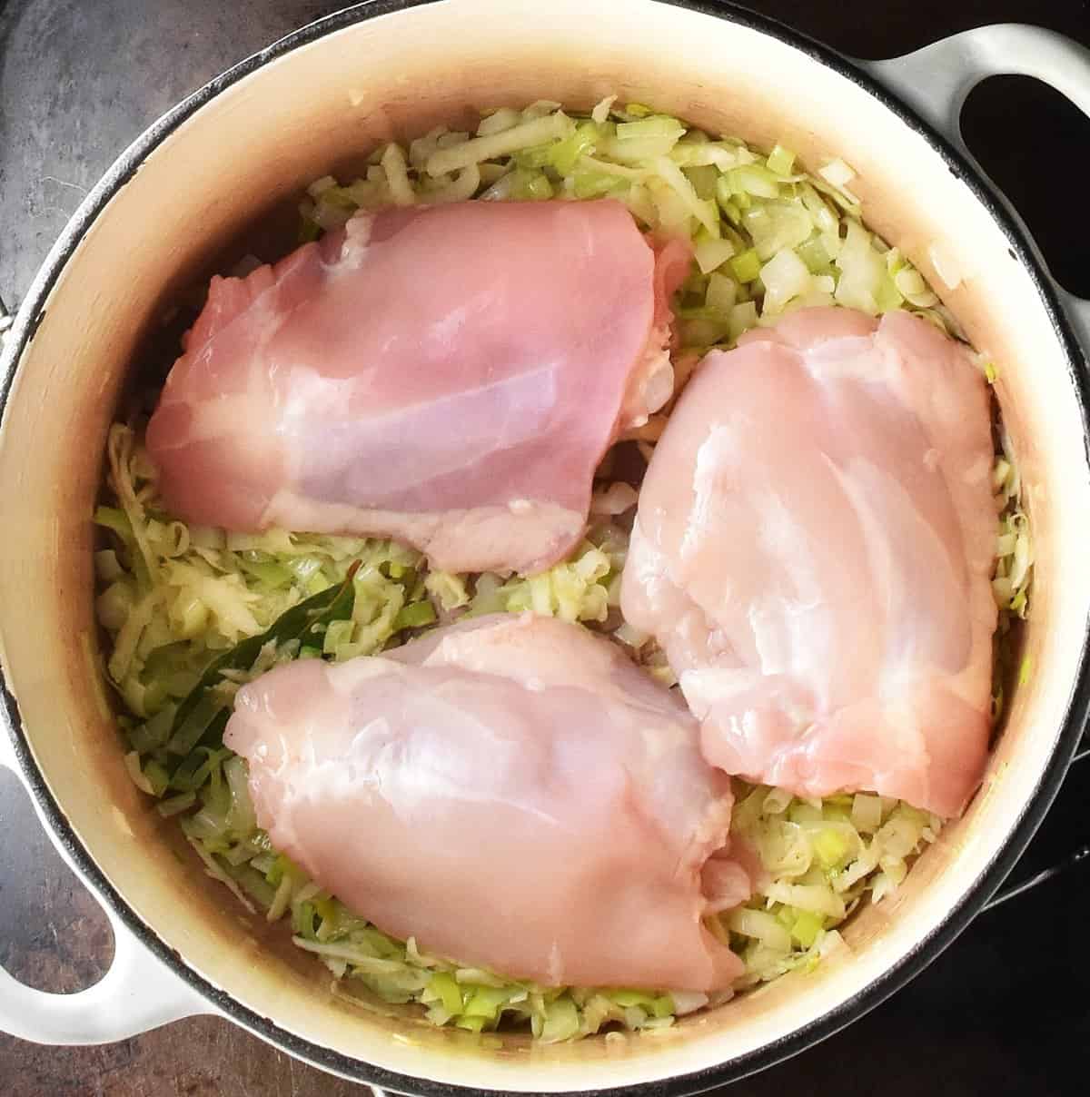 3 skinless chicken thighs on top of vegetables in white pot.