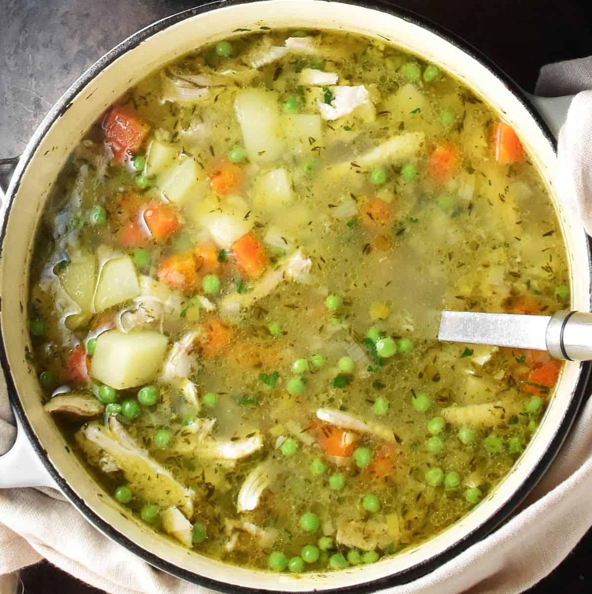 Top down view of chicken potato vegetable soup on white pot with ladle.