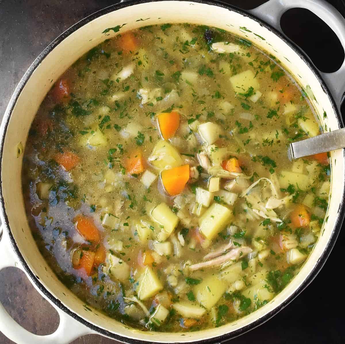 Top down view of Polish krupnik barley soup in white pot with ladle.