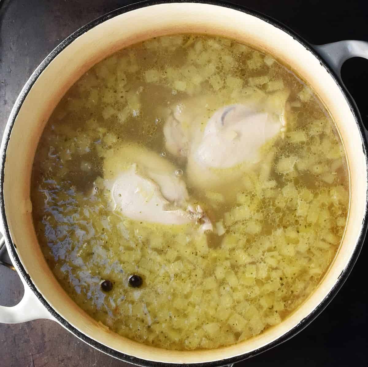 Top down view of 2 cooked chicken thighs in broth in white pot.