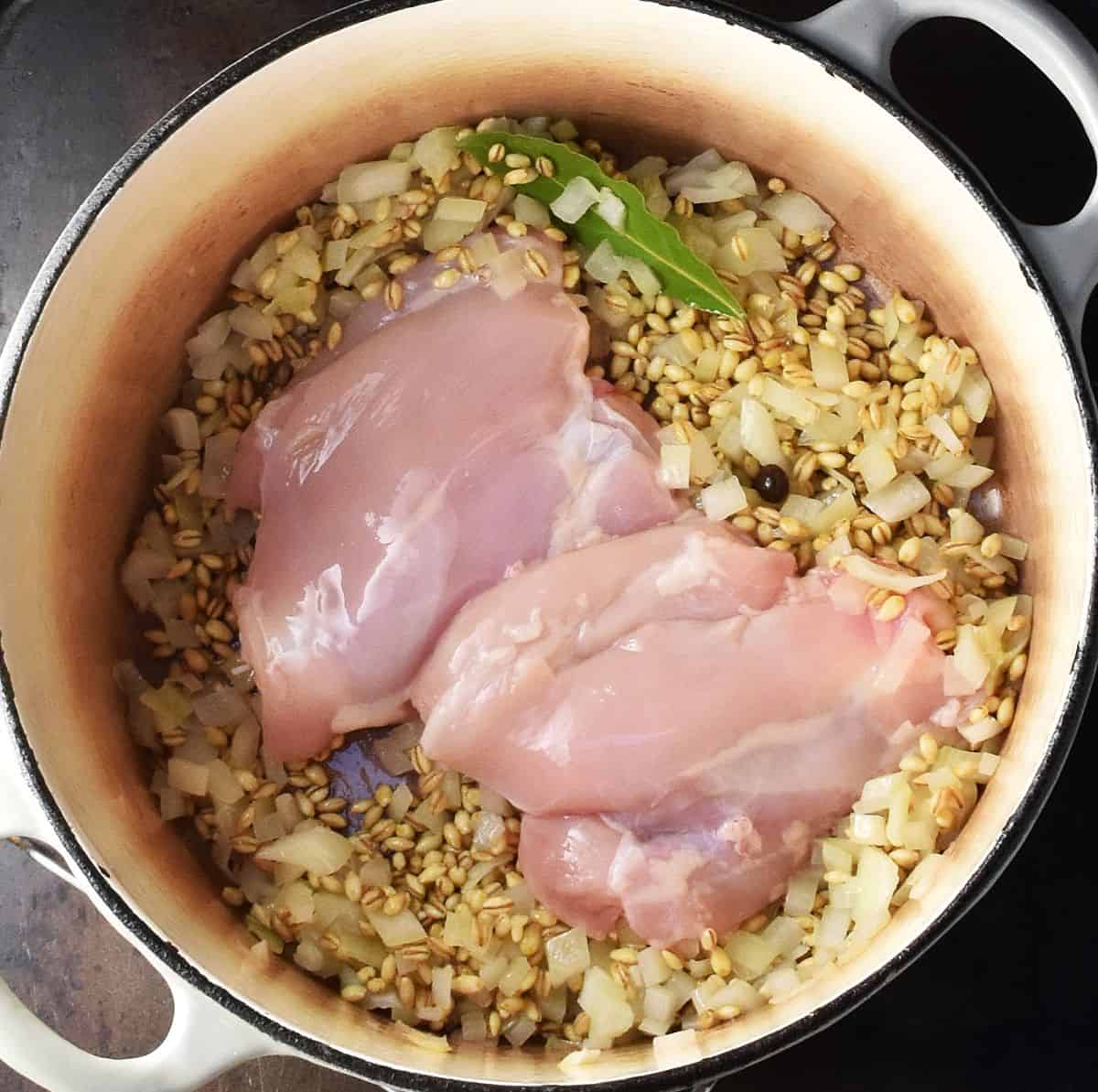 2 skinless chicken thighs with barley in white pot.