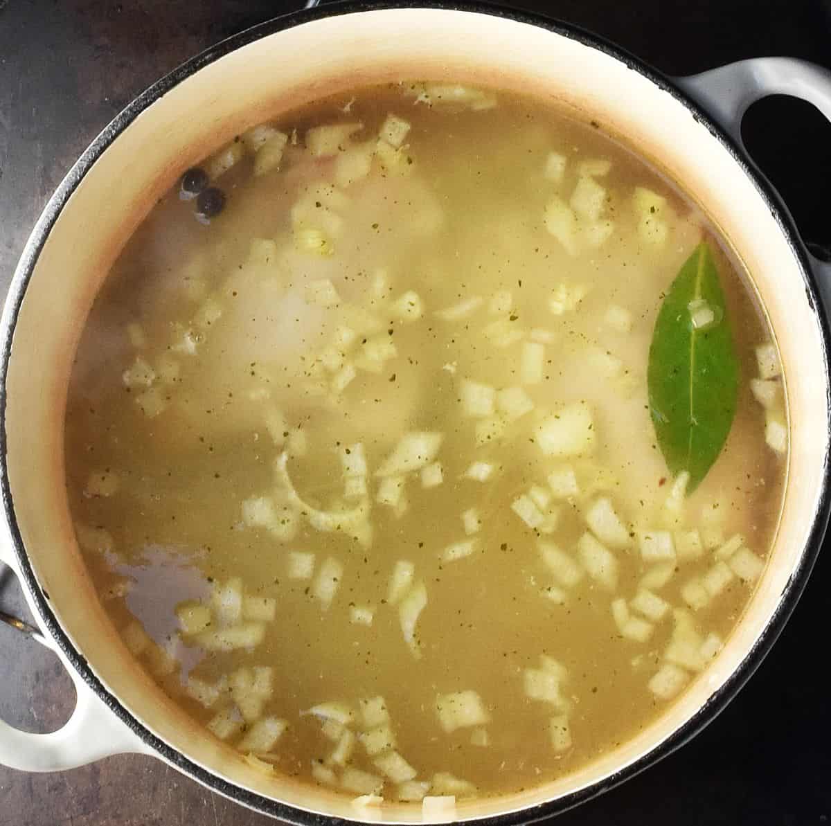 Chicken in broth with bay leaf in white pot.
