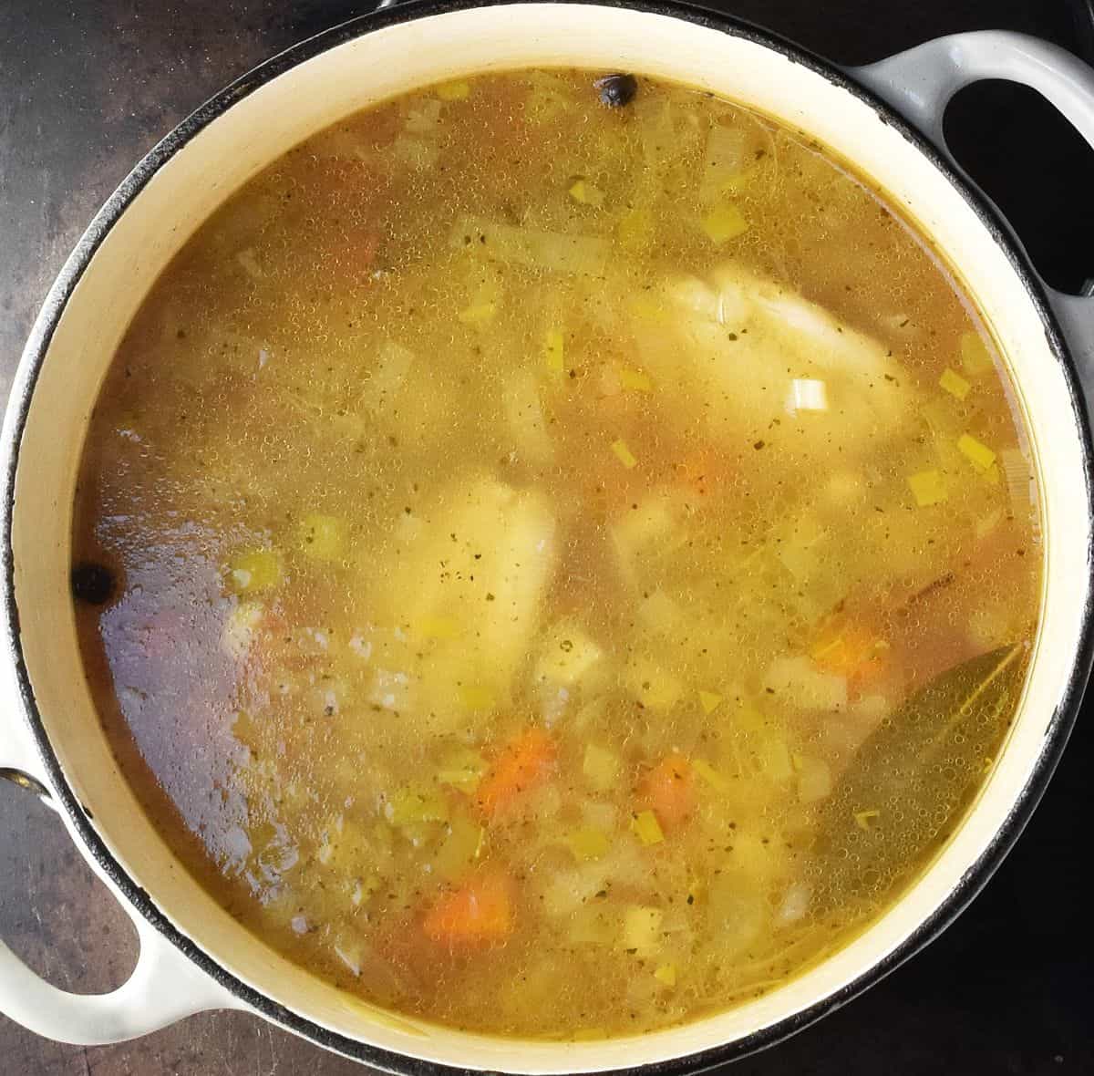 Chicken, barley and vegetables with broth in white pot.