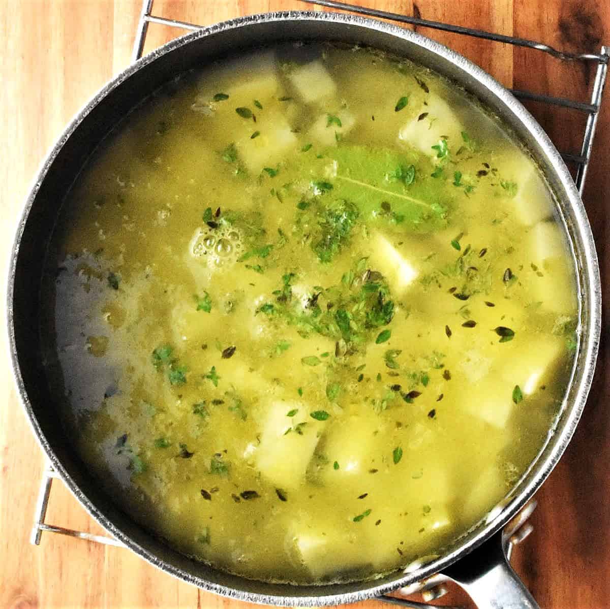 Top down view of soup with chunky vegetables and herbs in large pot.