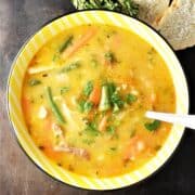 Top down view of turkey vegetable soup in yellow bowl with spoon.