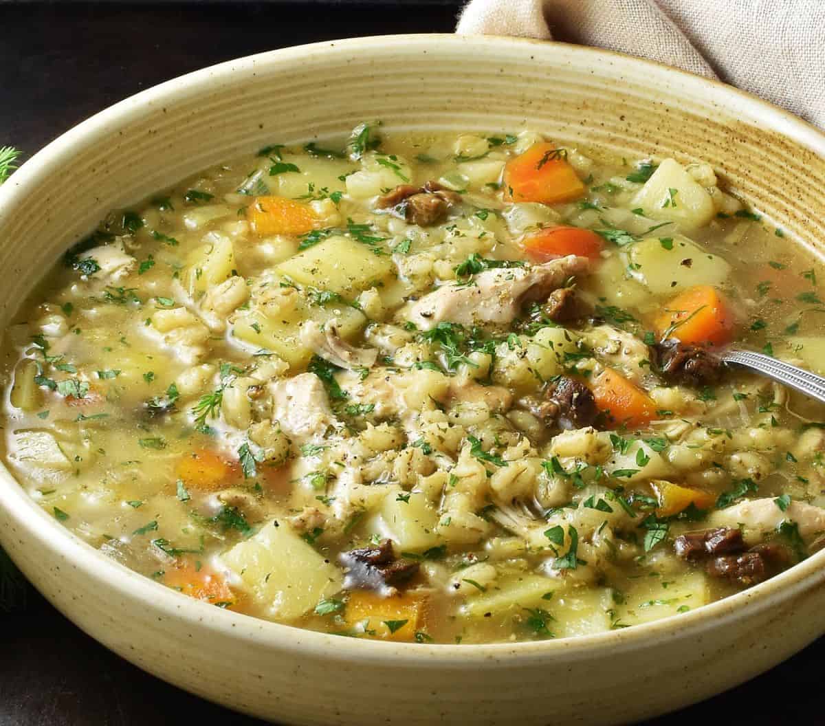 Side view of Polish barley krupnik soup in brown shallow bowl.