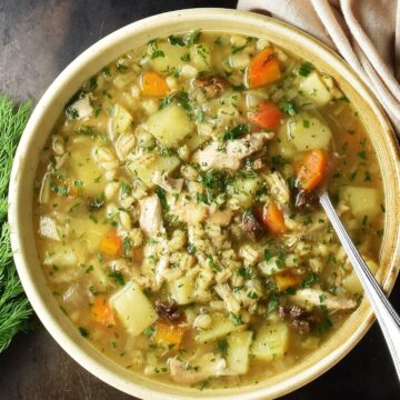 Top down view of Polish barley krupnik soup in brown bowl with spoon.