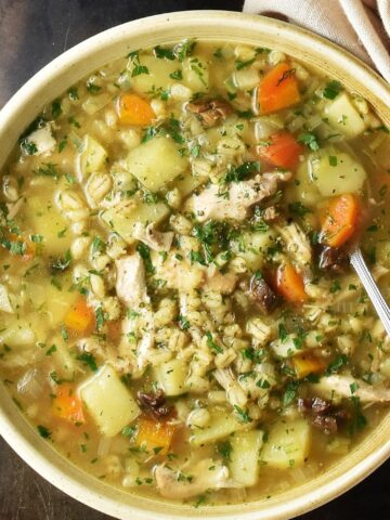 Top down view of Polish barley krupnik soup in brown bowl with spoon.