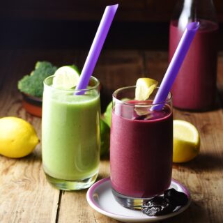 Purple and green broccoli smoothies with purple straws and lemon in background.