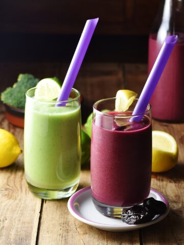 Purple and green broccoli smoothies with purple straws and lemon in background.