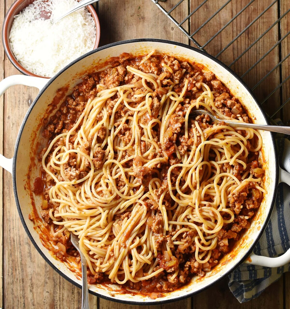 Spaghetti bolognese in large white shallow dish with grated cheese in small dish and rack at the top