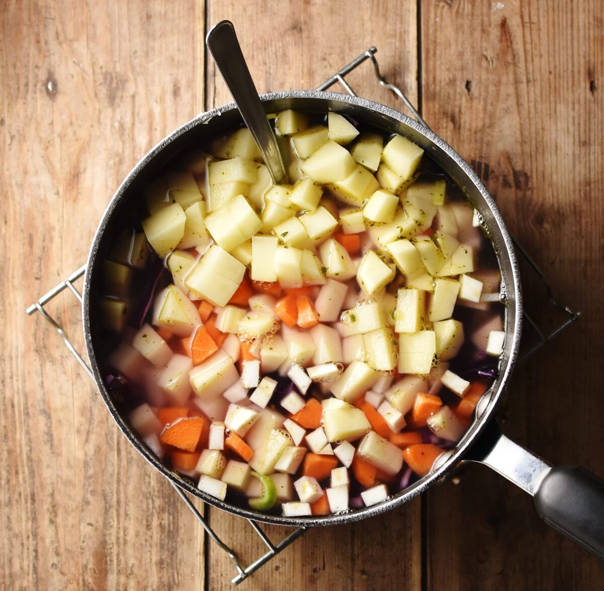 Cubed vegetables with water in large pot with spoon on top of rack.