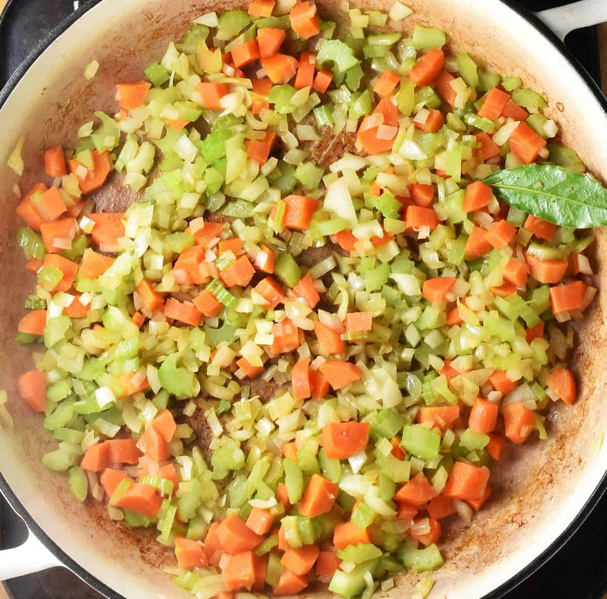 Chopped soffritto vegetables in shallow white pan.
