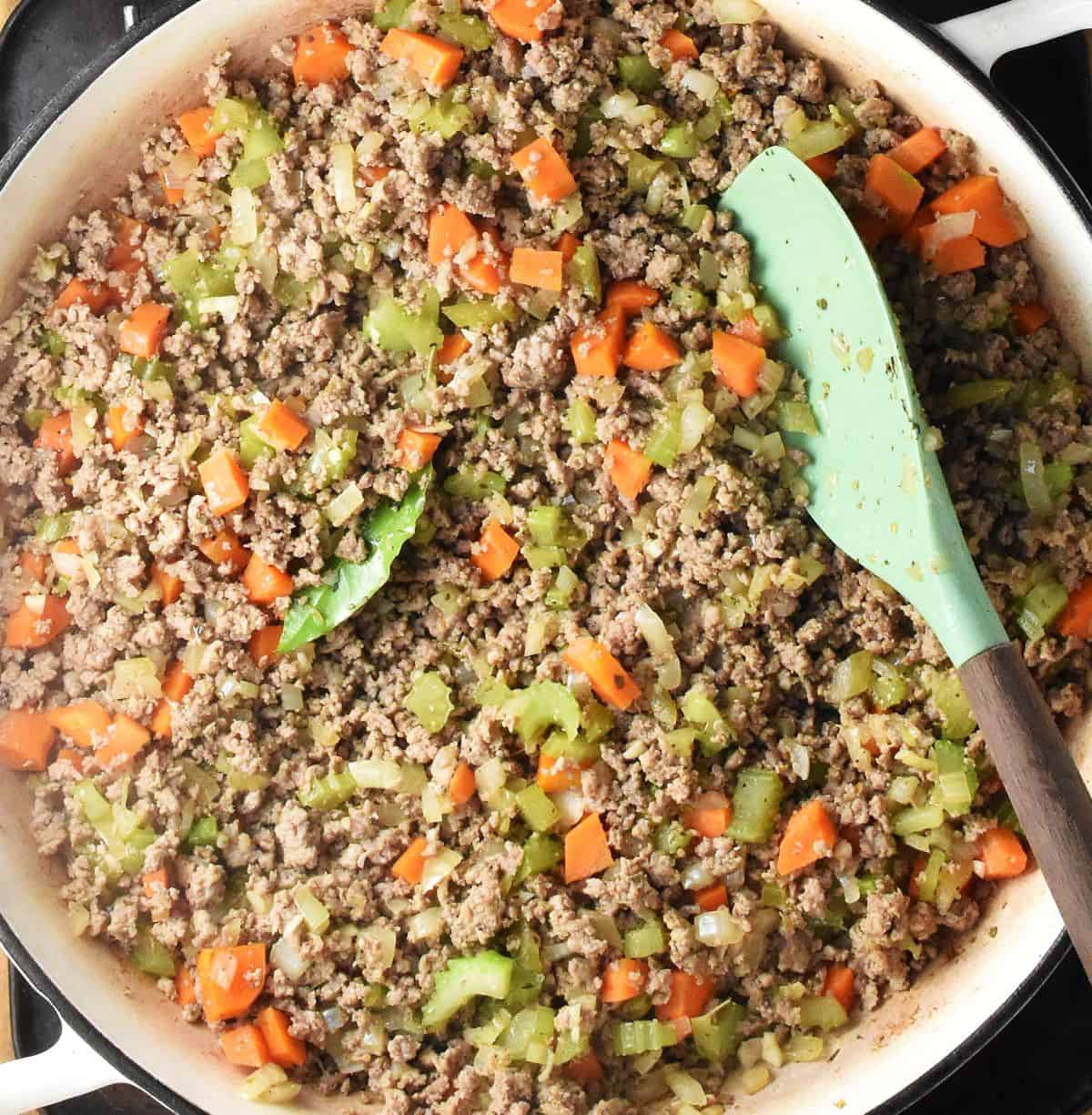 Ground turkey and chopped vegetables in large pan with spatula.