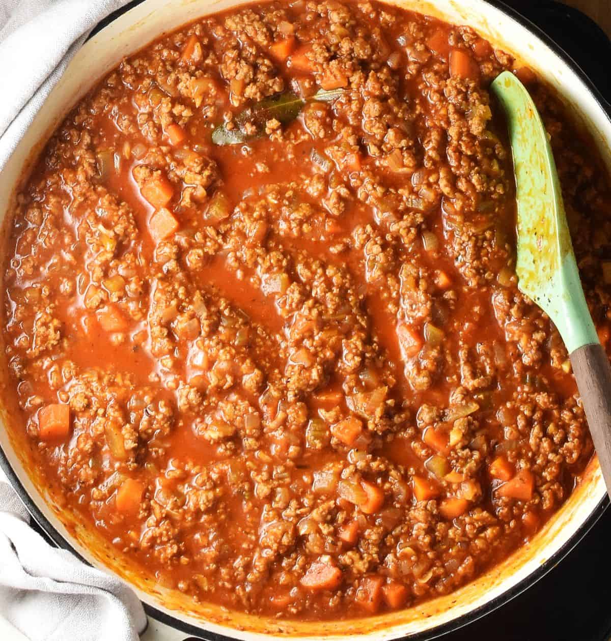 Top down view of turkey ragu pasta sauce in white shallow pan with spatula.