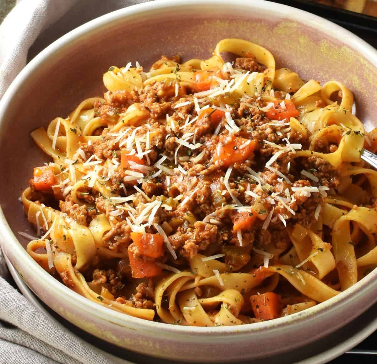 Side view of turkey bolognese with pasta in pink bowl.