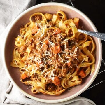 Top down view of turkey bolognese with pasta in pink bowl with fork.