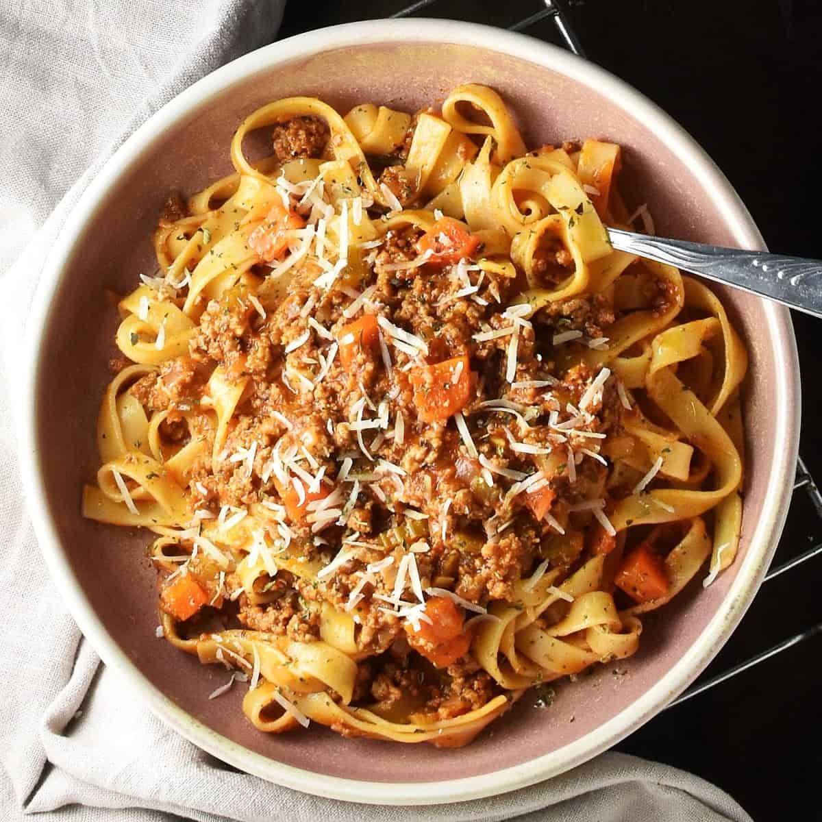 Top down view of turkey ragu with pasta in pink bowl with fork.