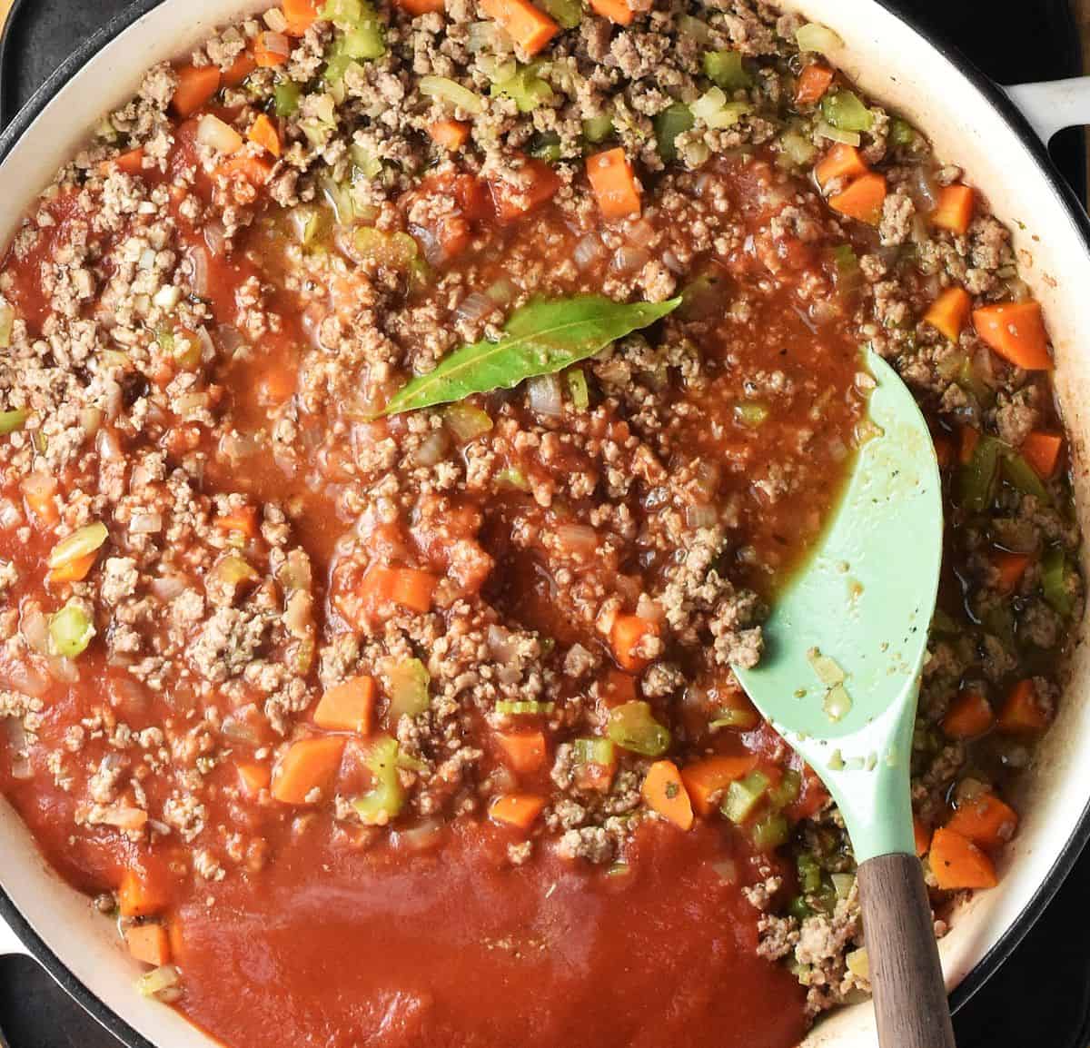Ground turkey with passata in white pan with spatula.