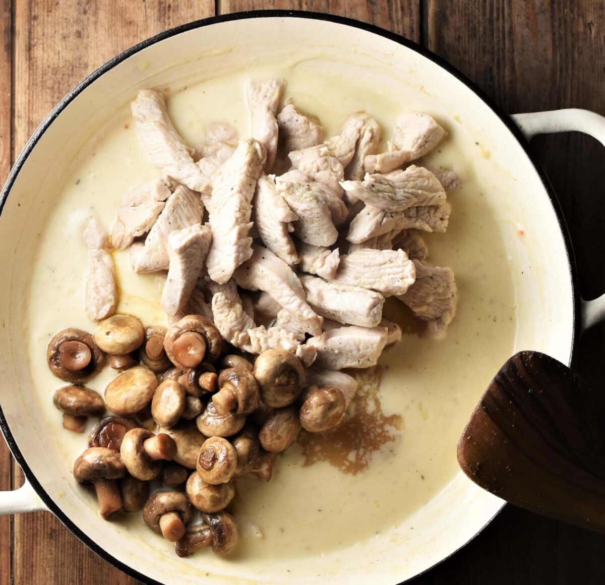 Mushrooms and turkey strips with creamy sauce in large white pan with spatula in bottom right corner.
