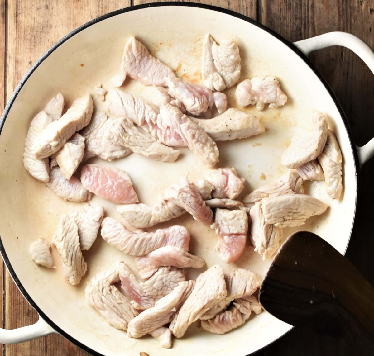 Turkey strips in large white pan with spatula in bottom right corner.