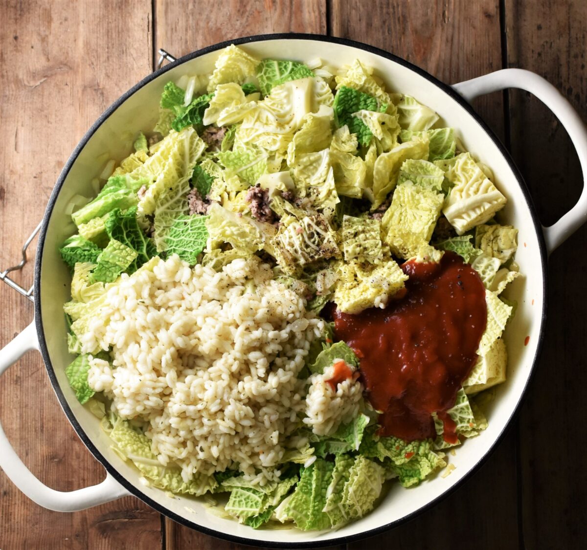 Chopped cabbage, rice and tomato passata in large shallow white pan.