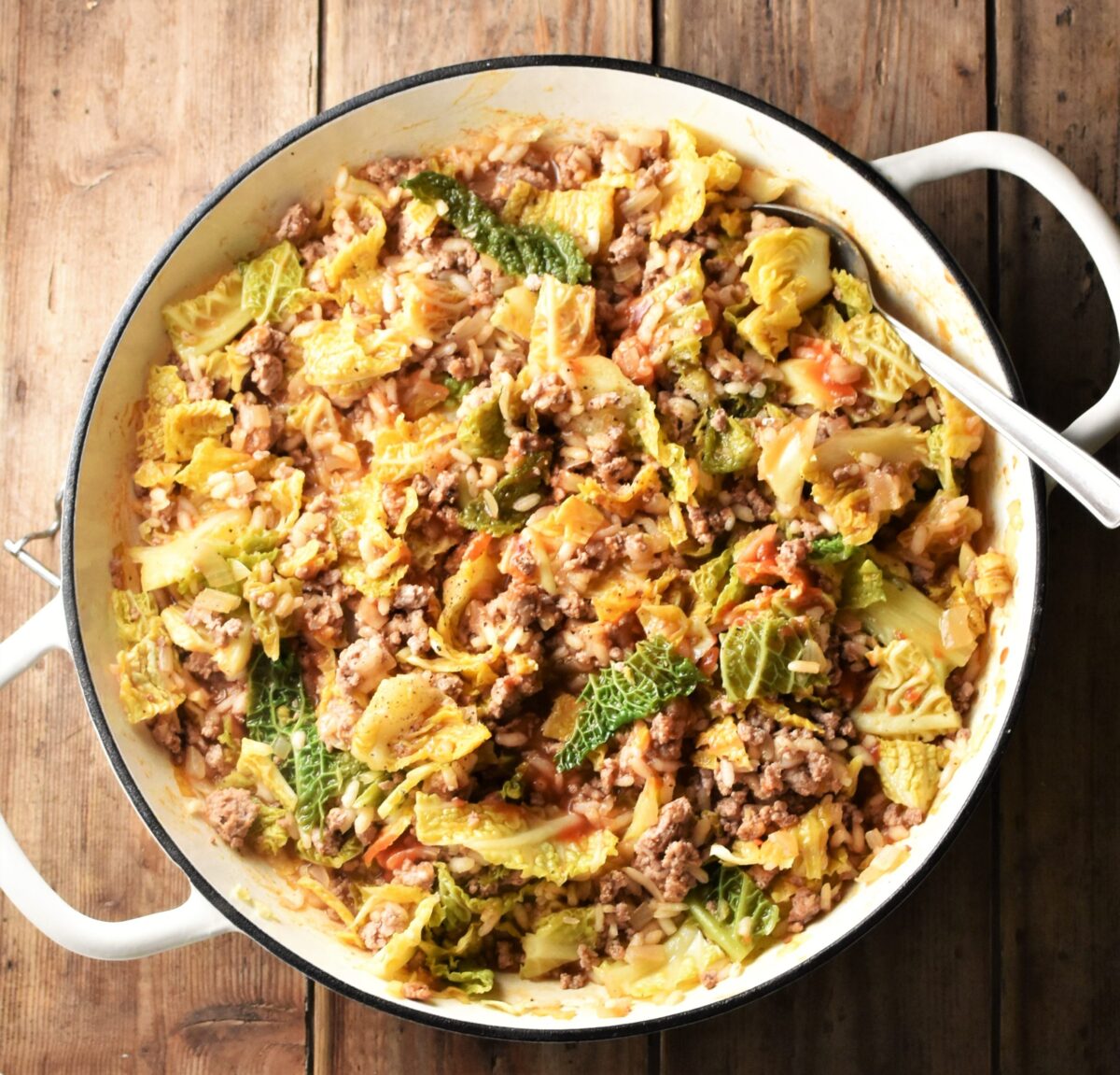 Chopped cabbage, ground meat and rice in large, shallow, white dish with spoon.