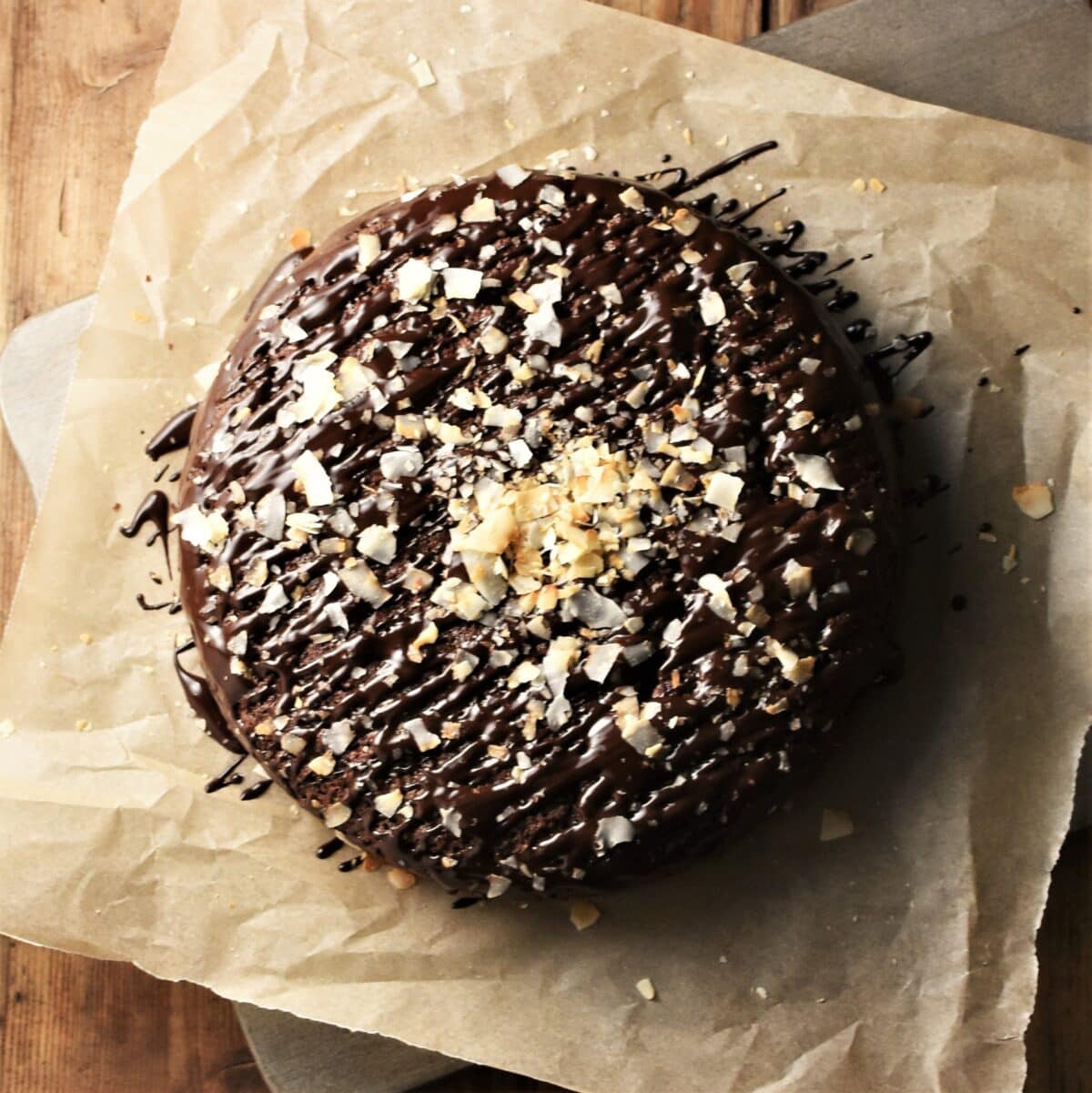 Chocolate cake with chocolate drizzle and coconut flakes on top of paper.