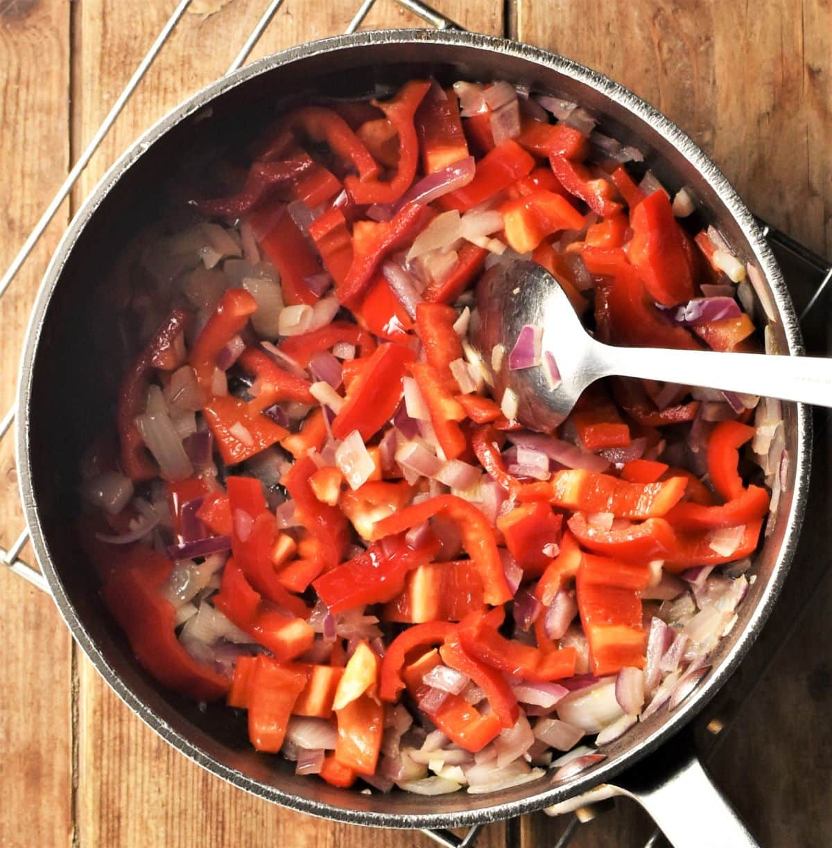 Sauteeing red onion and red pepper in large pot with spoon.