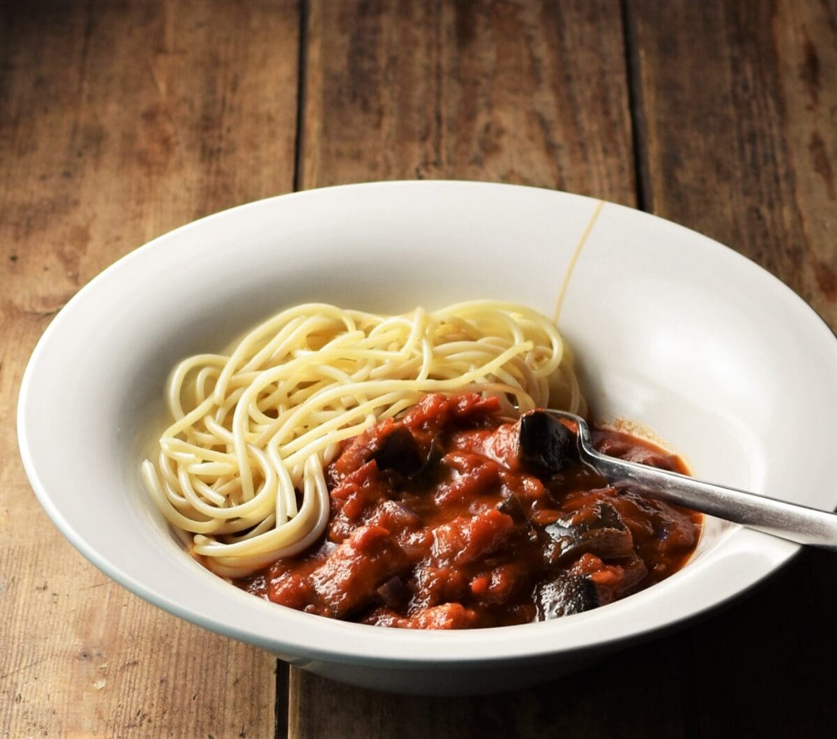 Eggplant tomato sauce with spaghetti in white bowl with fork.