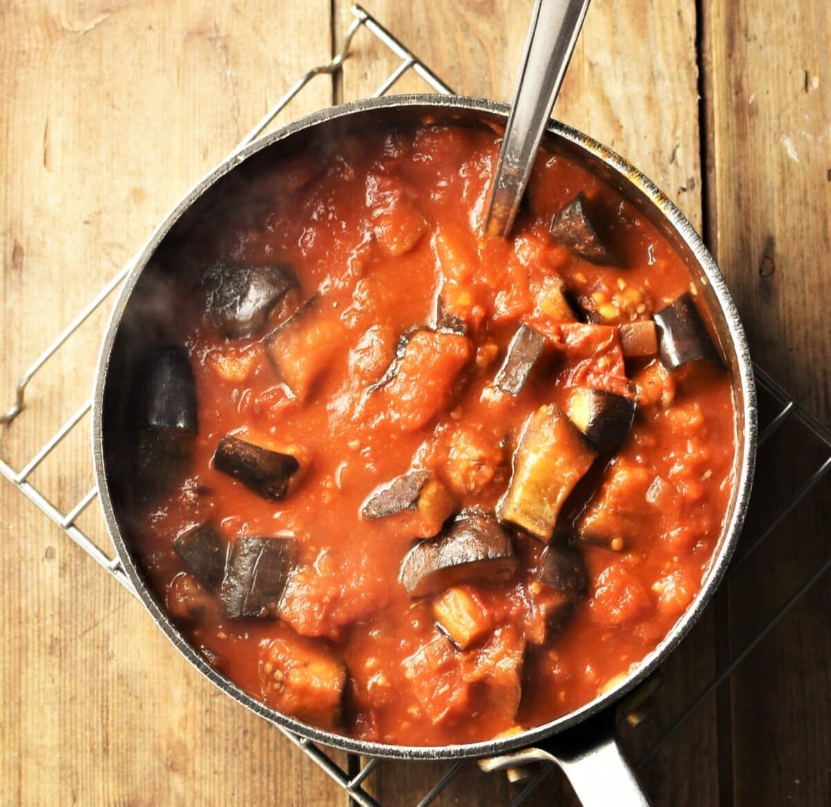Top down view of eggplant and tomato sauce in large pot with spoon.