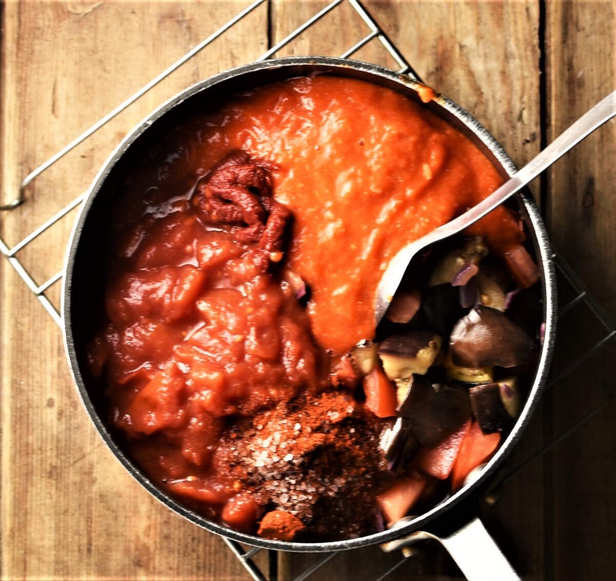 Chopped eggplant, tomatoes and pepper puree in pot with spoon.