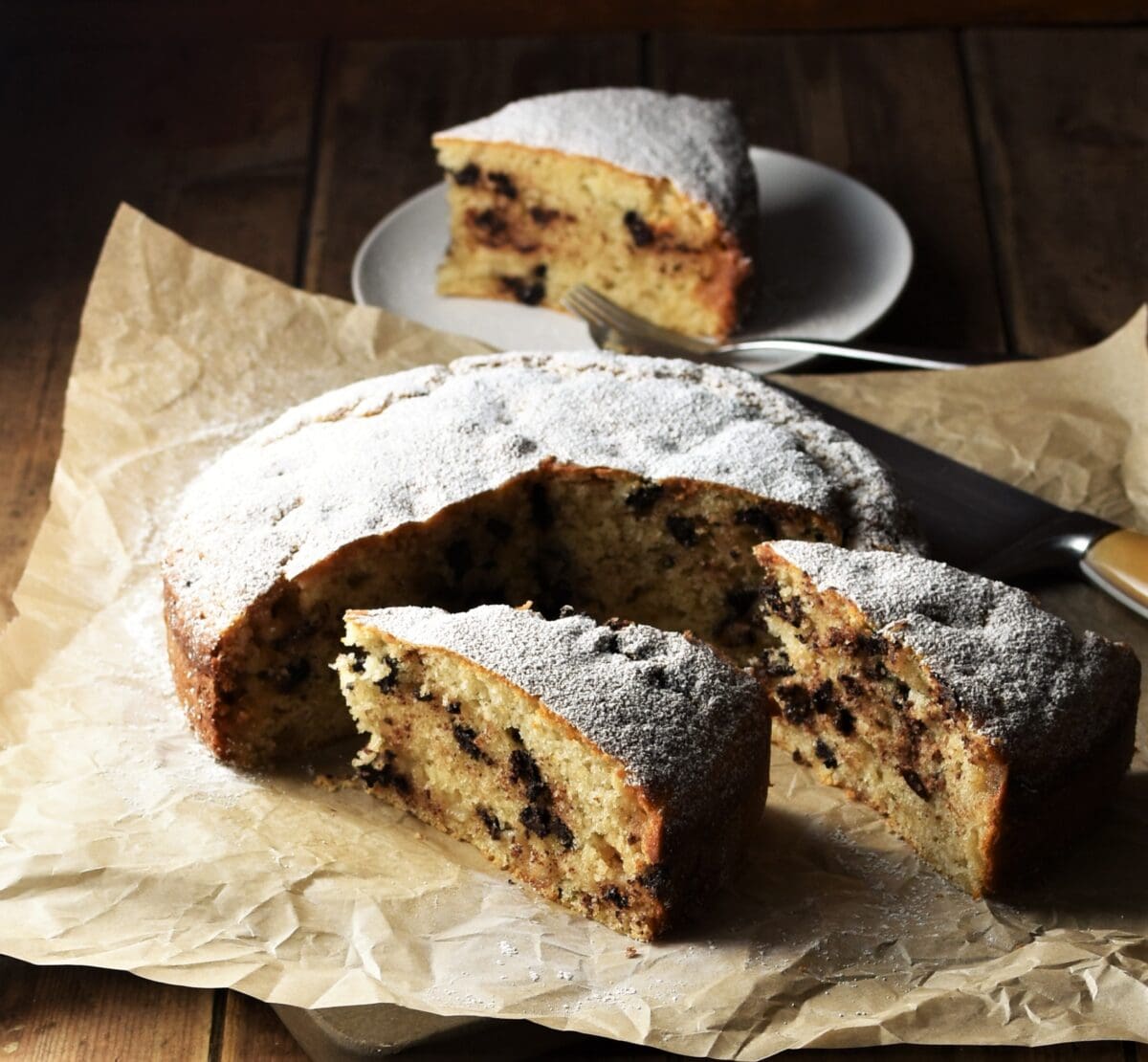 Slices of marzipan cake on top of paper with cake in background.