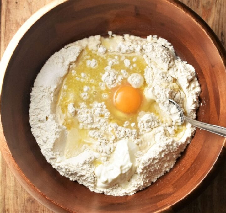 Flour and egg in large wooden bowl with spoon.