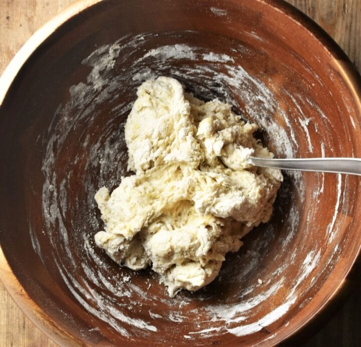 Making pierogi dough in large wooden bowl with spoon.