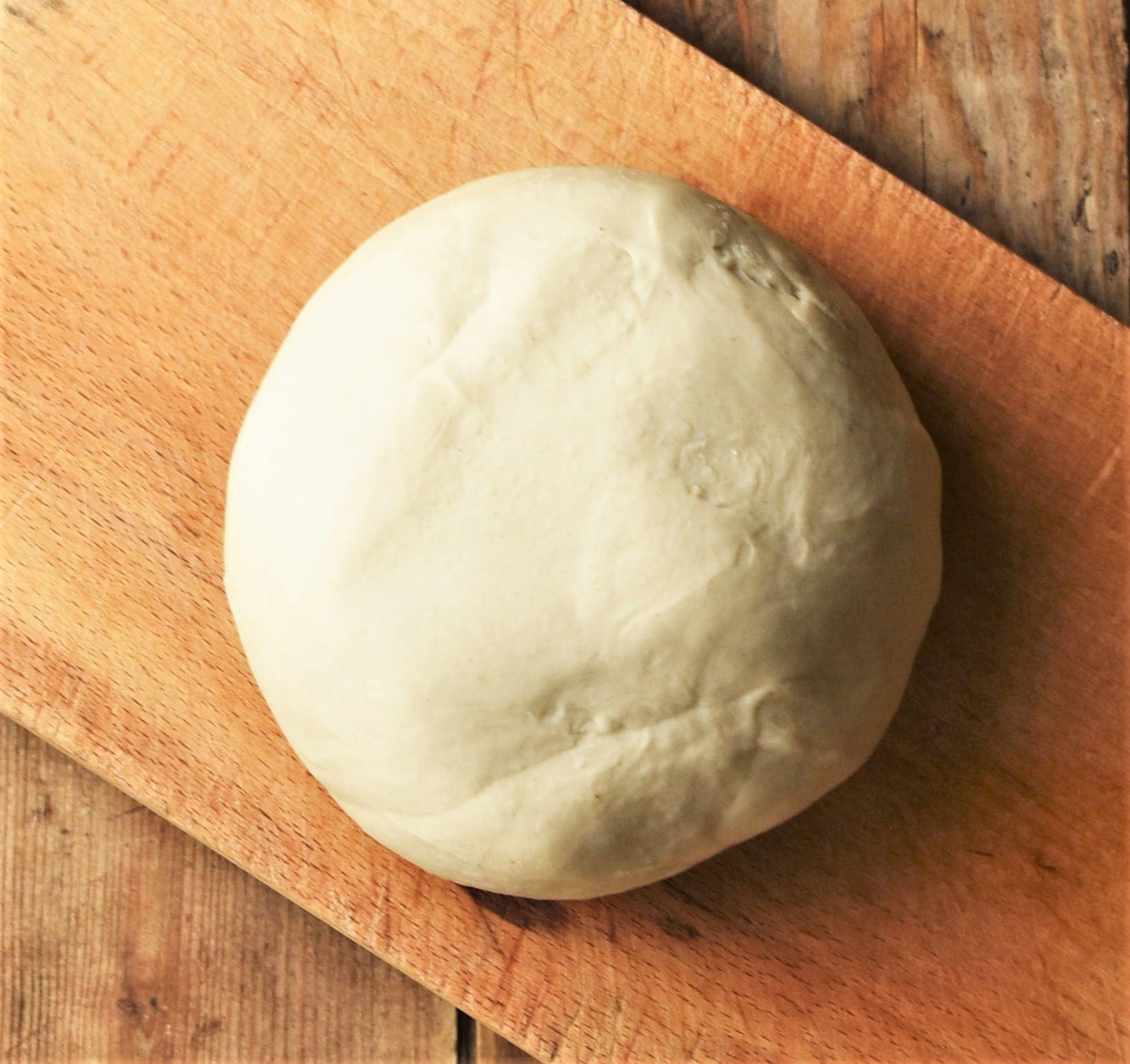 Round smooth pierogi dough on top of wooden board.