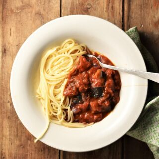 Chunky eggplant tomato sauce with spaghetti in white bowl with fork.