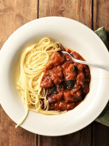 Chunky eggplant tomato sauce with spaghetti in white bowl with fork.