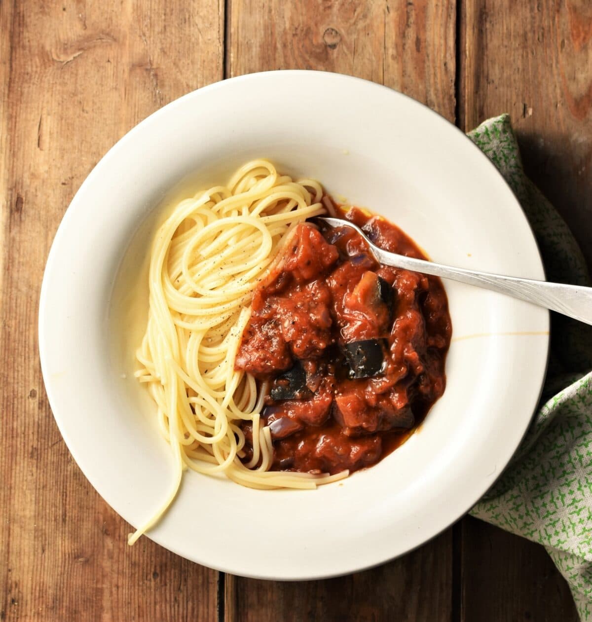 Chunky eggplant tomato sauce with spaghetti in white bowl with fork.