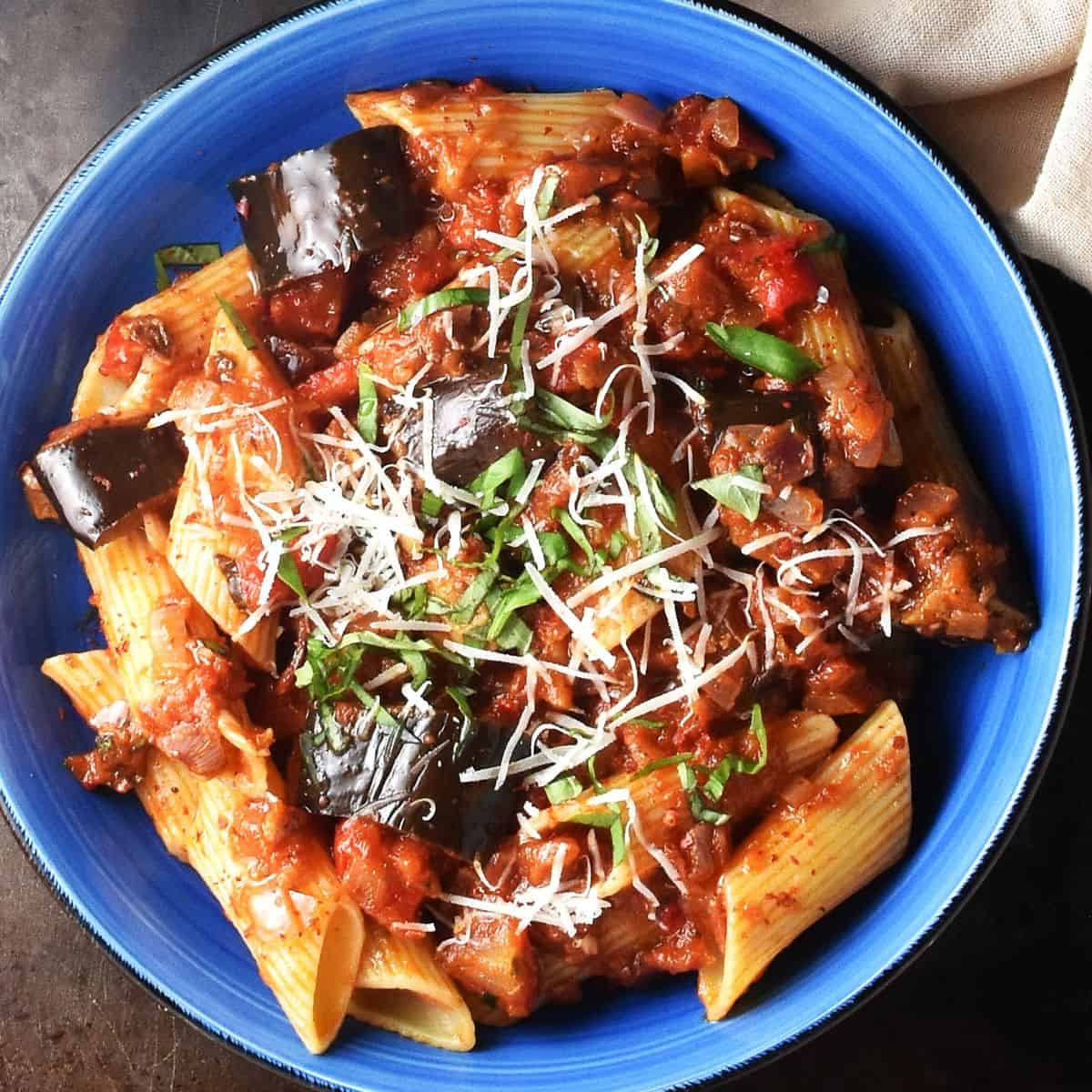 Top down view of eggplant pasta sauce with pasta in blue bowl.