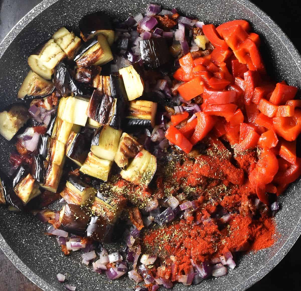 Chunks of roasted eggplant, chopped red pepper and onion in large pan.