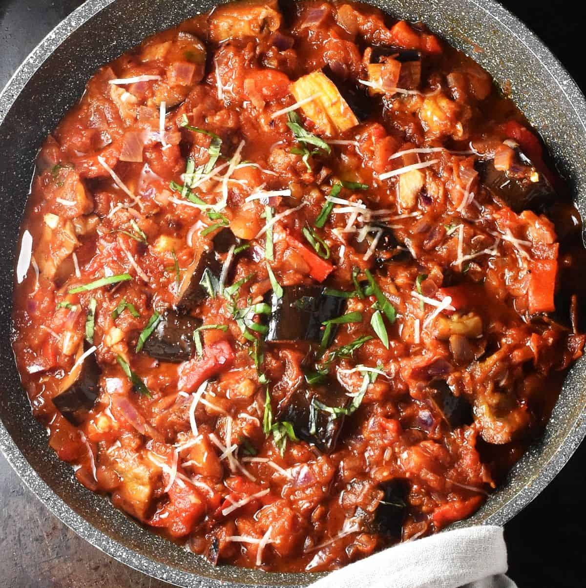 Top down view of chunky eggplant in tomato sauce with herbs on top in pan.