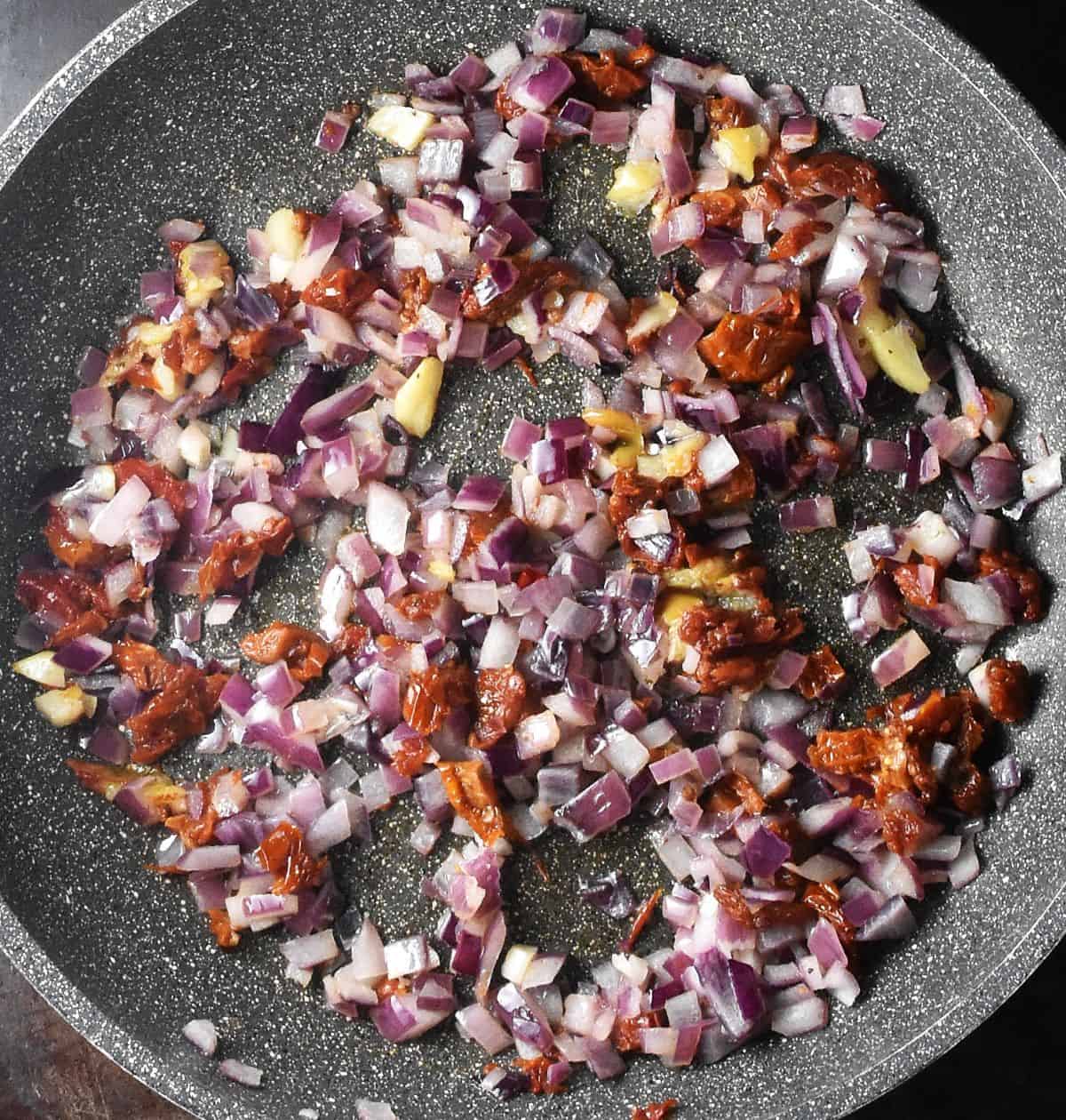 Chopped red onion and sundried tomatoes in large pan.
