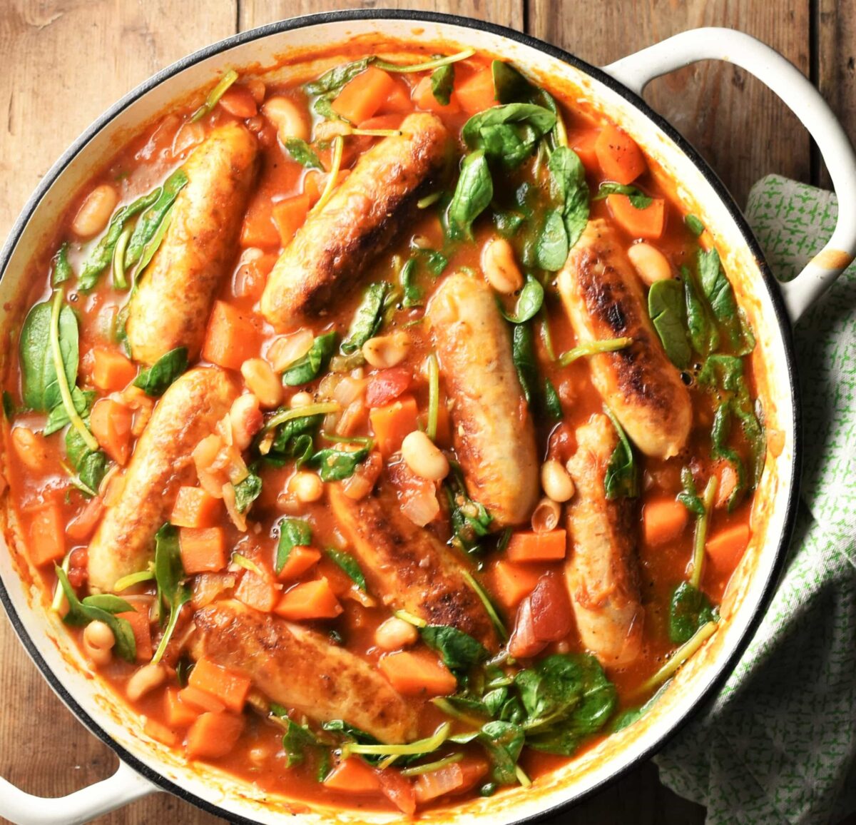 Beans and sausages with vegetables in large shallow white dish.