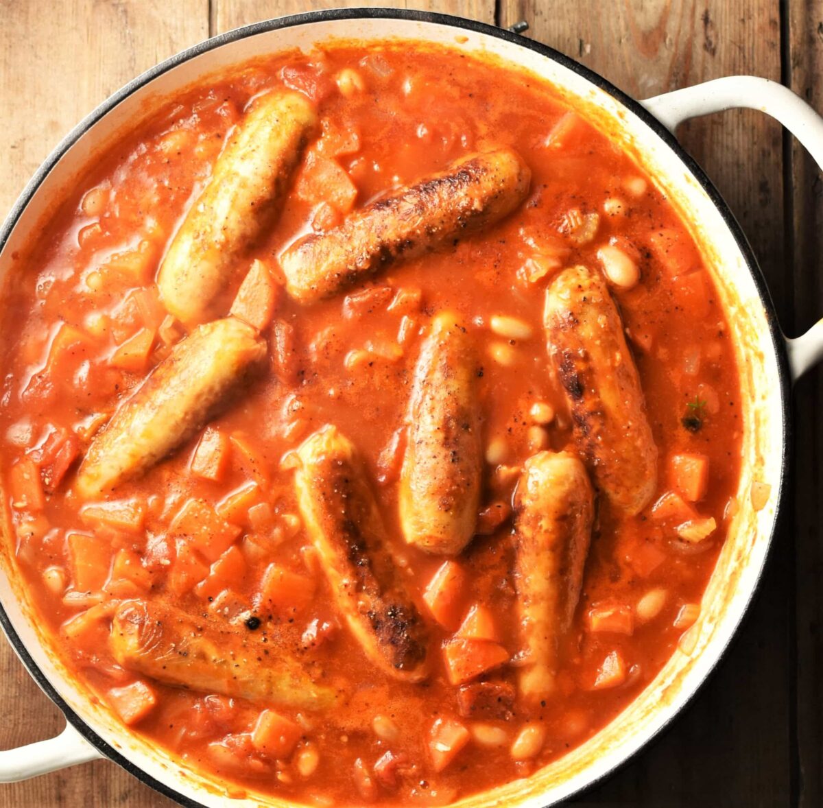 Sausages and beans in tomato sauce in shallow white pan.