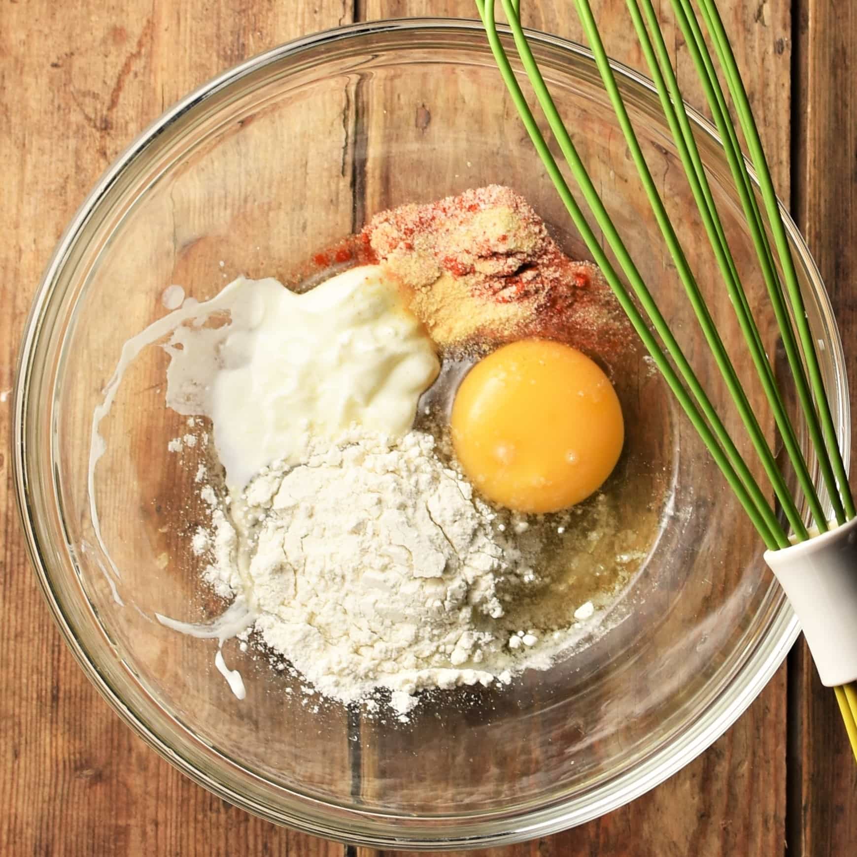 Flour, egg, yogurt and spices in mixing bowl with green whisk.