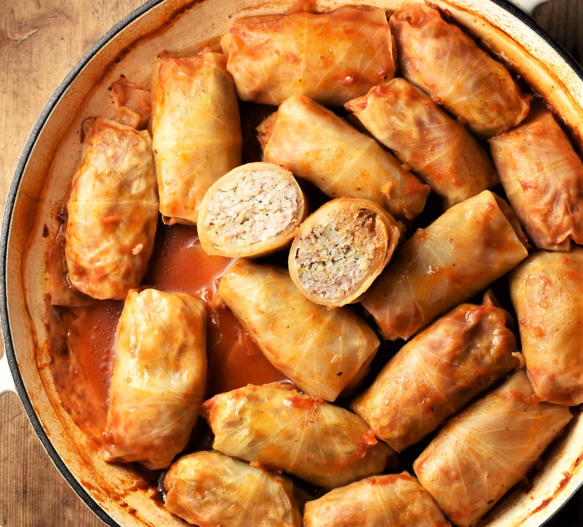 Top down view of cabbage rolls in tomato sauce in large white shallow pan.