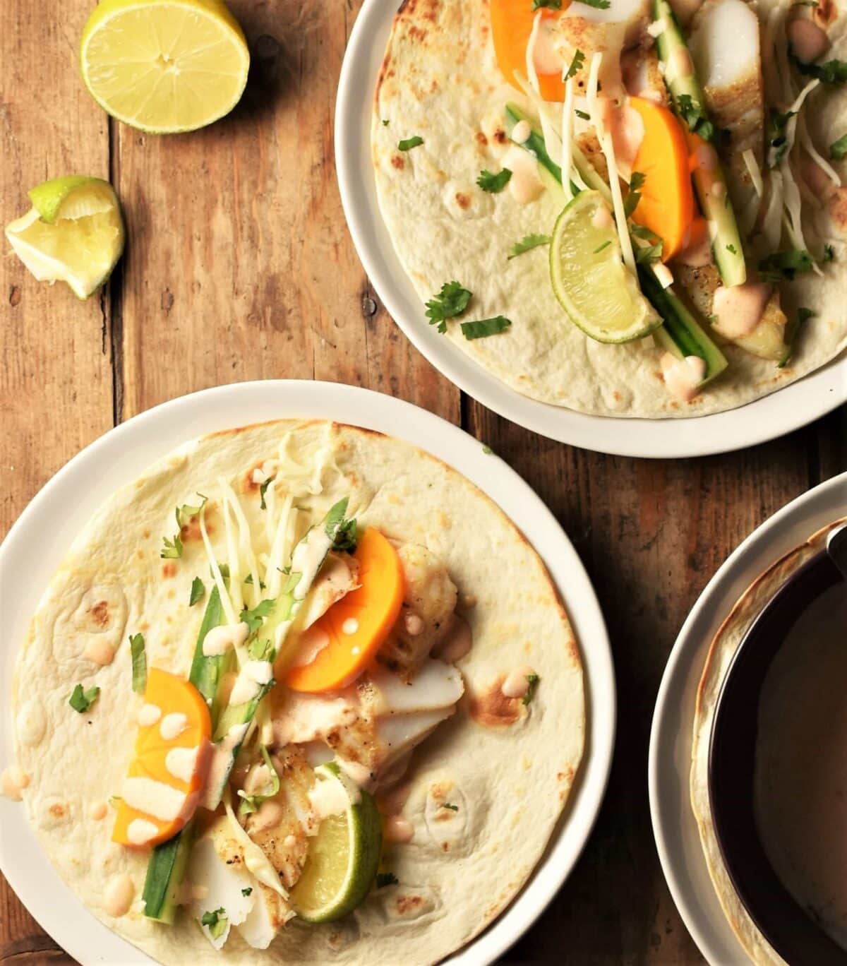 2 fish tacos with vegetables and sauce on plates with lime in background.