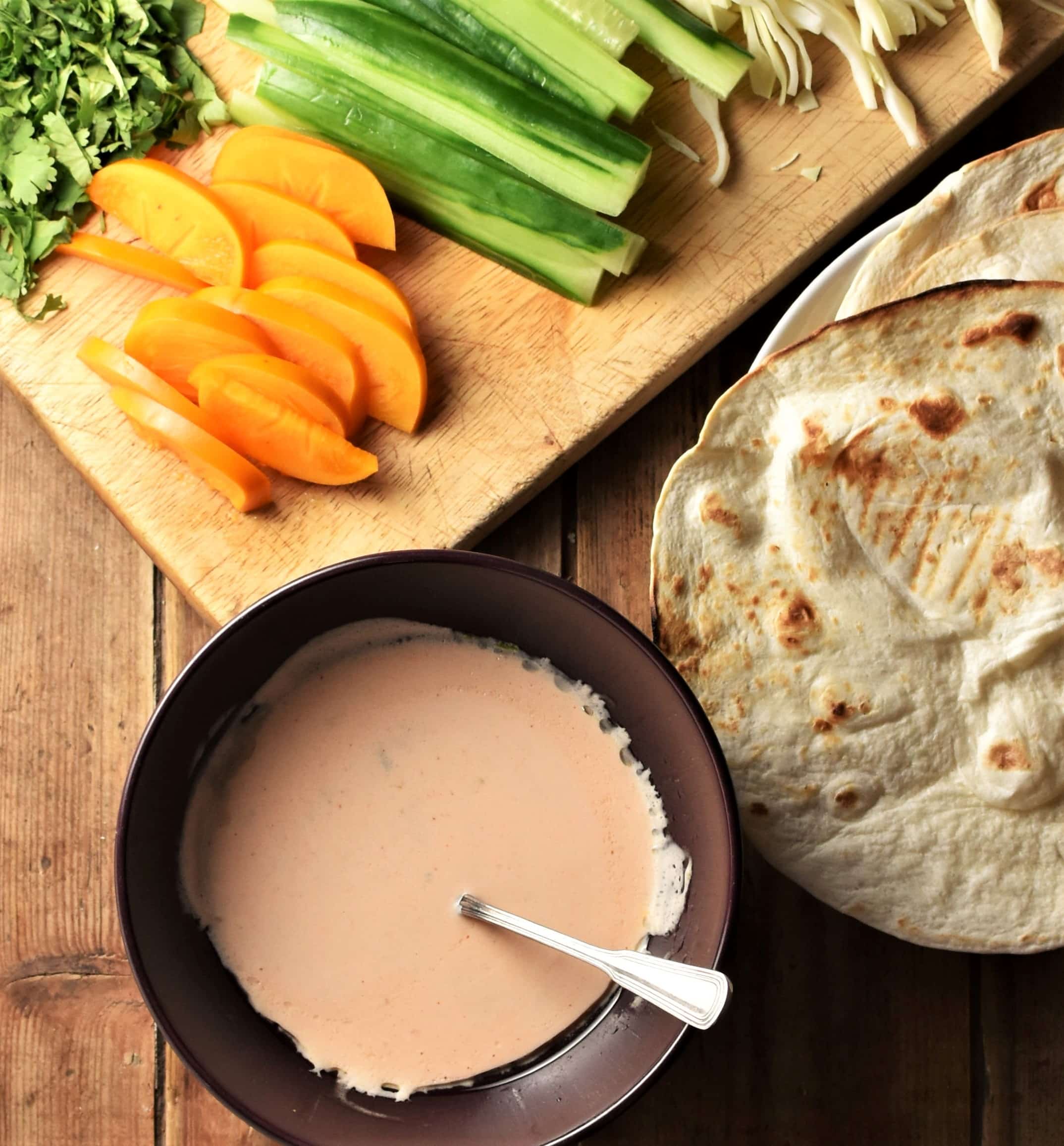 Creamy sauce, tortillas and chopped fruit and begetables on top of wooden board.