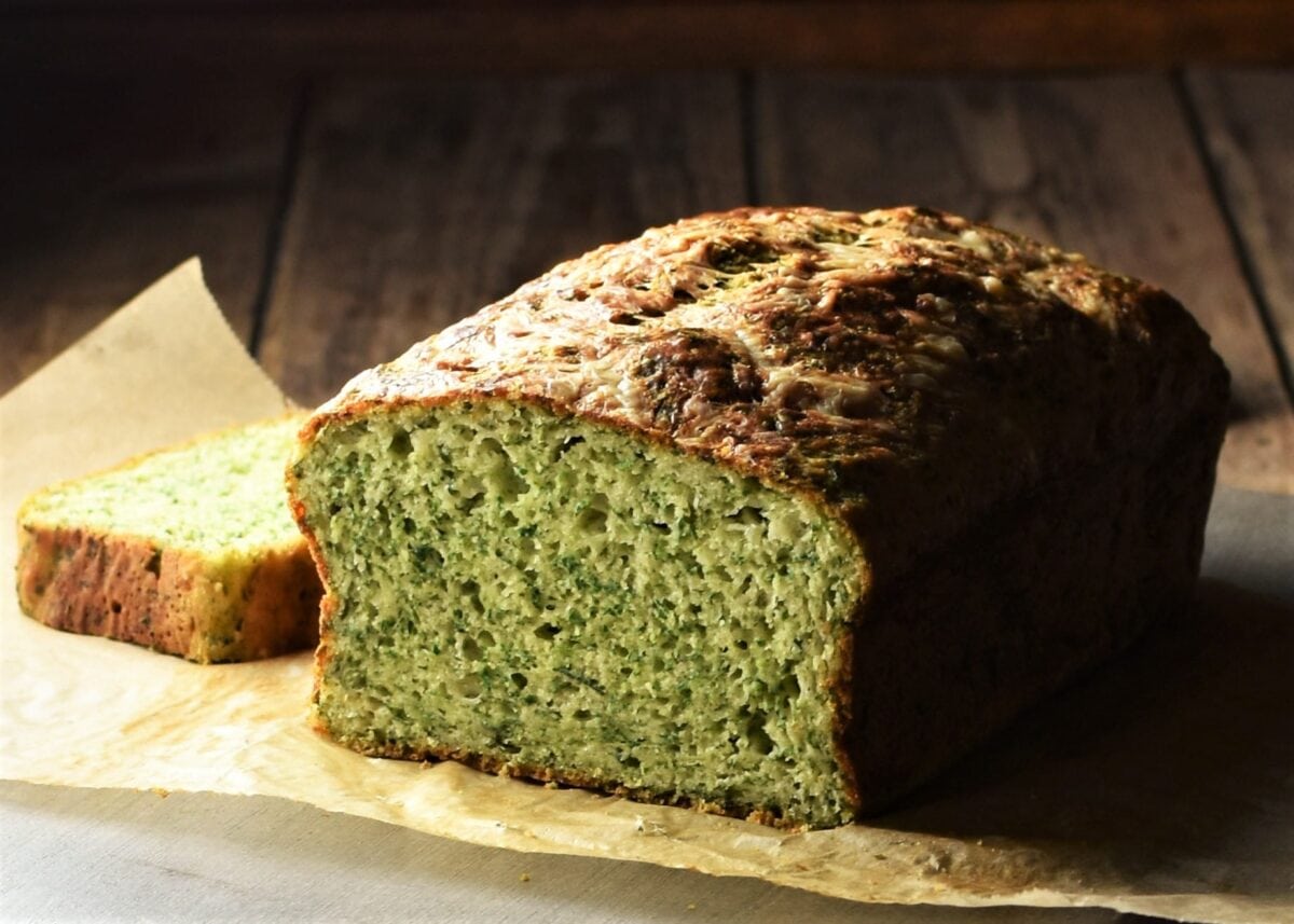 Side view of spinach bread with slice behind on top of parchment.